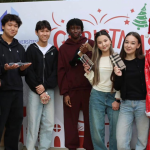 Students posing together at a Christmas event on campus, holding gifts and standing next to a person dressed as Santa Claus.